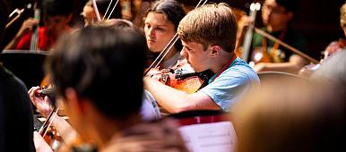 Image of students reading sheet music and playing violins.